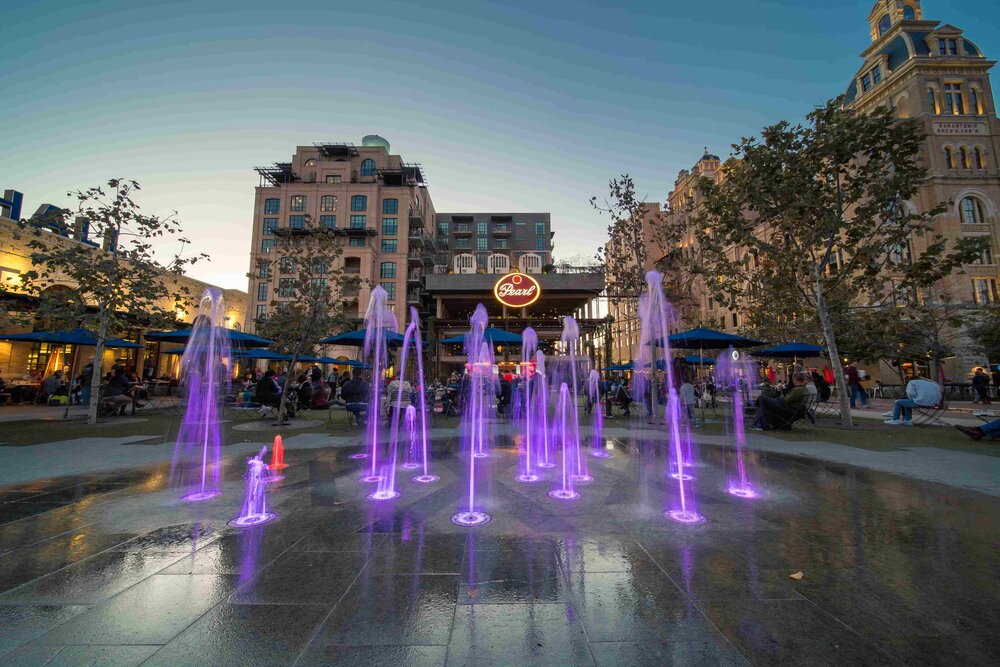 Colorful splash pad fountains at an urban park during twilight