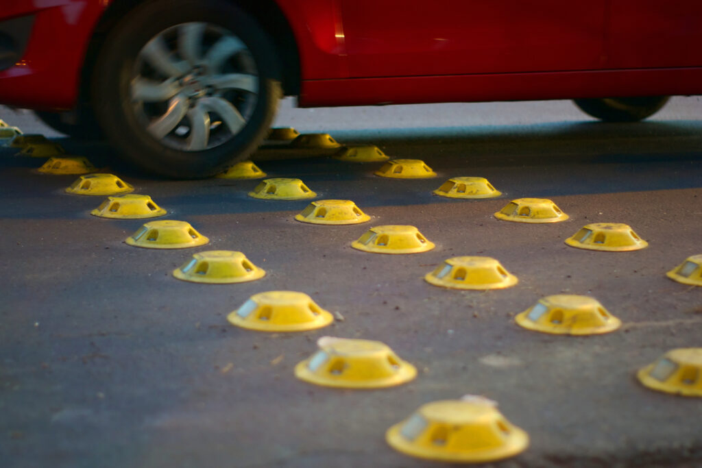 Close-up of a vehicle passing over reflective road studs, illustrating what is a traffic calming device and how it works.